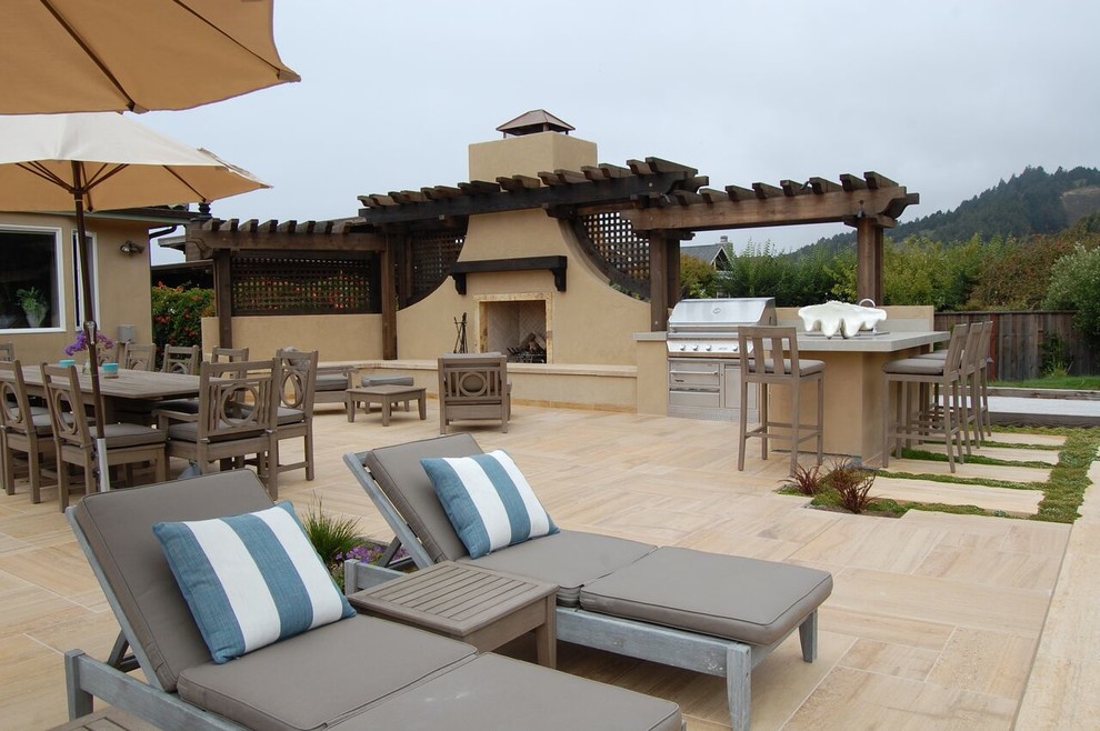 На фото: большой двор на заднем дворе в средиземноморском стиле с покрытием из плитки и местом для костра без защиты от солнца