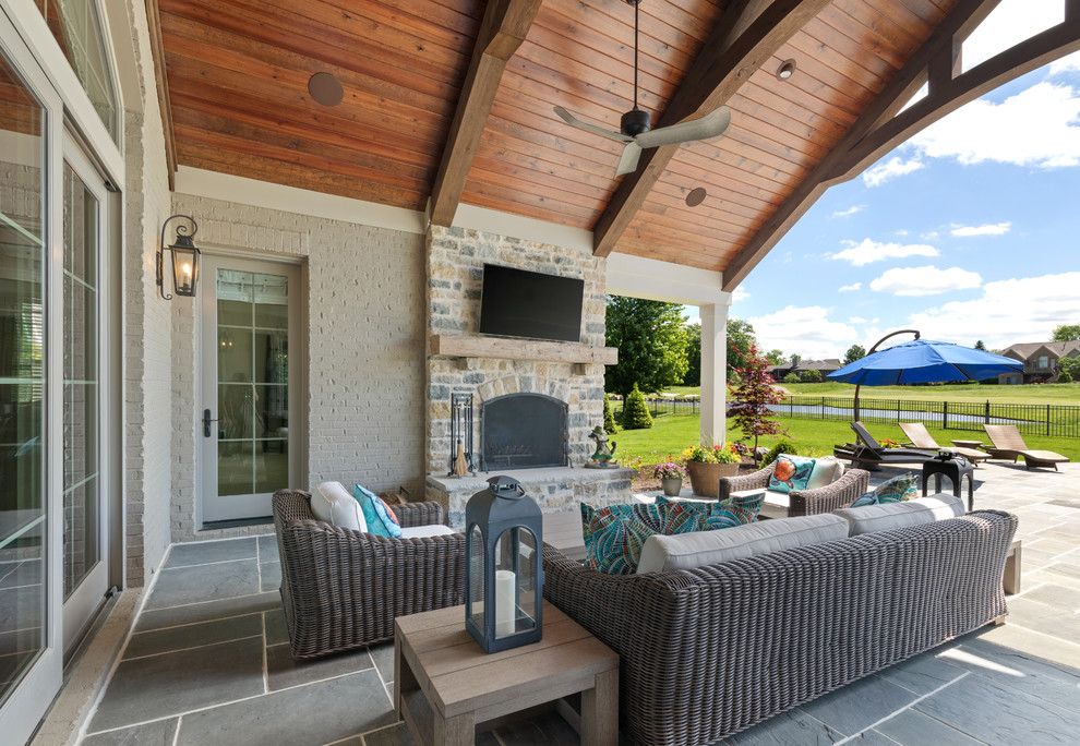Large elegant backyard stone patio photo in Cincinnati with a fireplace and a roof extension
