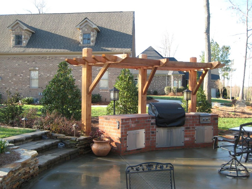 Large classic back patio in Charlotte with an outdoor kitchen, concrete paving and a pergola.