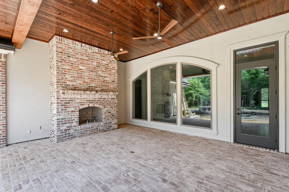 Example of a large transitional backyard brick patio design in New Orleans with a fireplace and a roof extension