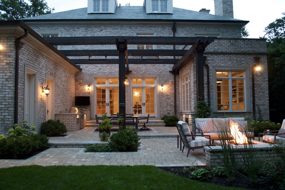 This is an example of a large classic back patio in Chicago with an outdoor kitchen, natural stone paving and a pergola.