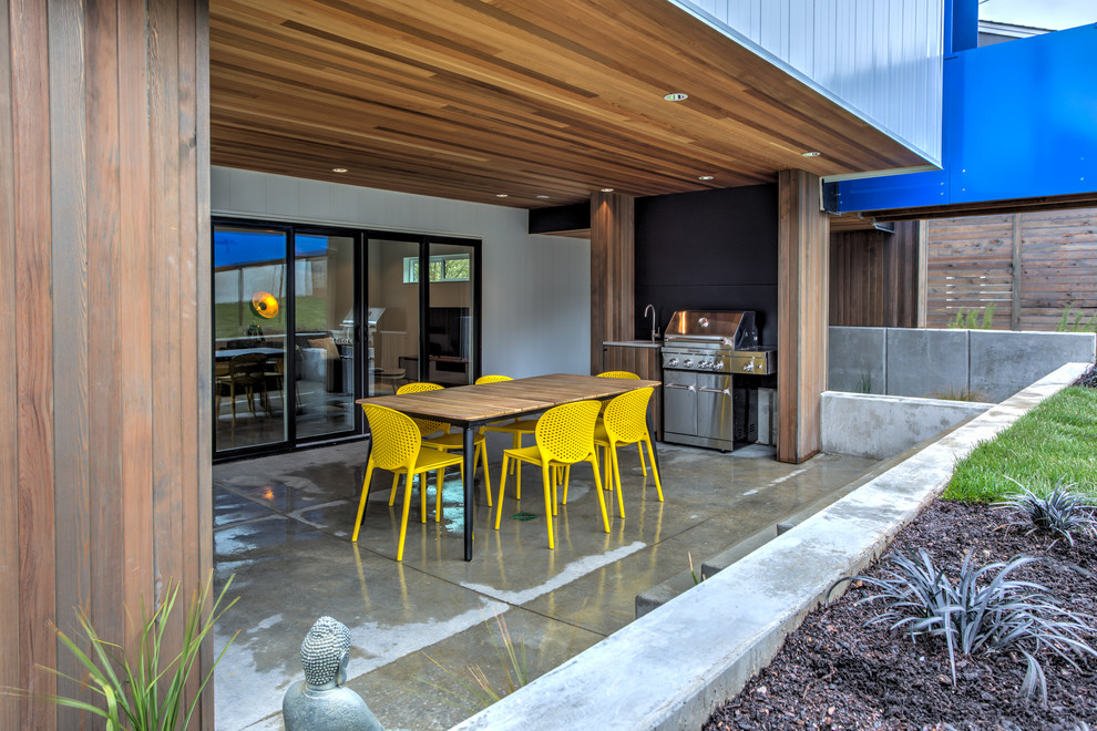 This is an example of a medium sized contemporary front patio in Seattle with an outdoor kitchen, concrete slabs and an awning.