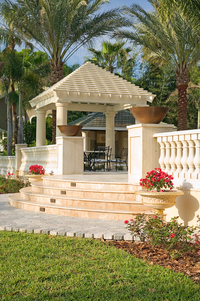 Example of a large island style backyard stone patio design in Tampa with a fire pit and a pergola