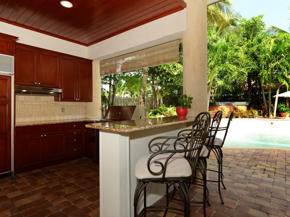 Large world-inspired back patio in Miami with an outdoor kitchen, brick paving and a roof extension.