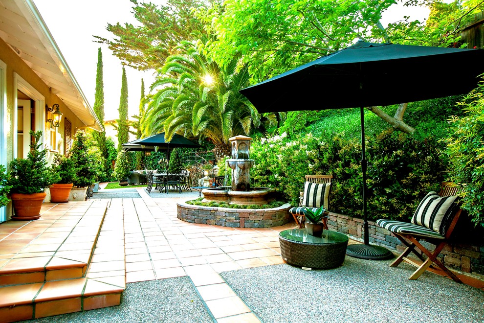 Immagine di un ampio patio o portico mediterraneo dietro casa con fontane, piastrelle e un gazebo o capanno