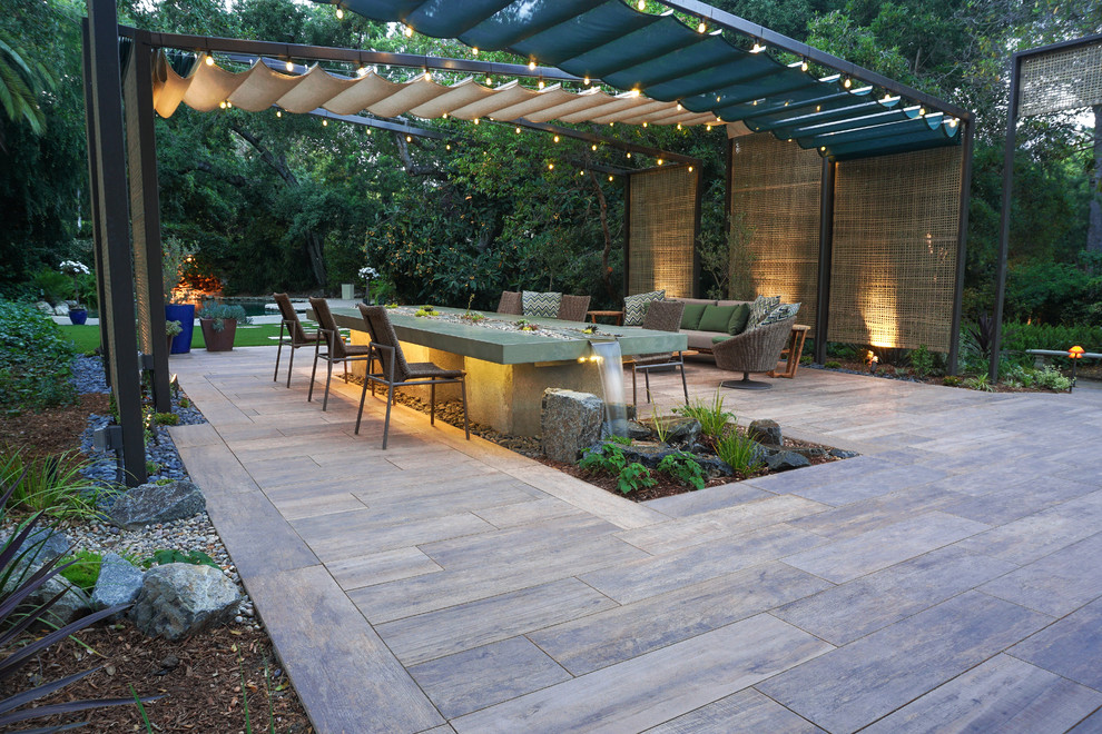 Contemporary back patio in Los Angeles with a water feature, natural stone paving and a pergola.