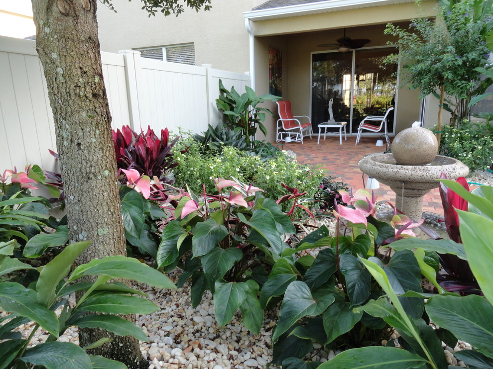 Foto di un patio o portico tropicale di medie dimensioni e dietro casa con fontane, pavimentazioni in mattoni e un tetto a sbalzo