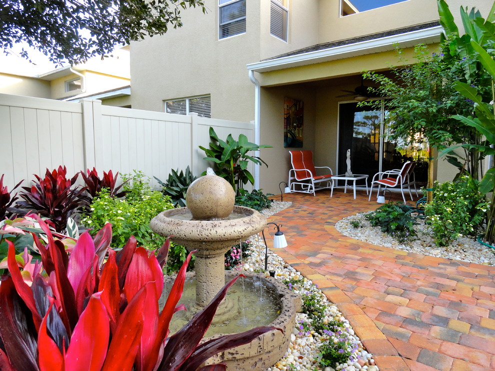 Immagine di un patio o portico tropicale dietro casa e di medie dimensioni con pavimentazioni in mattoni, fontane e un tetto a sbalzo
