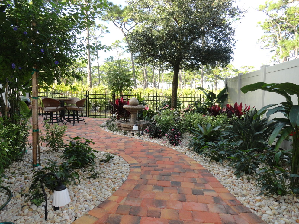 Diseño de patio tropical de tamaño medio en patio trasero y anexo de casas con adoquines de ladrillo y fuente
