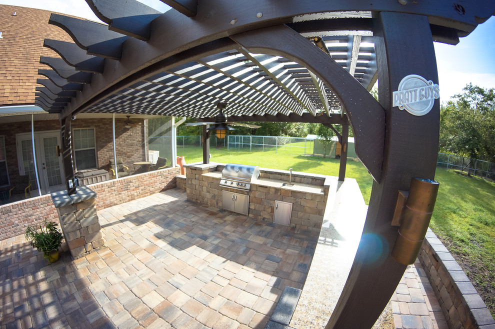 Modelo de patio tradicional grande en patio trasero con cocina exterior, adoquines de piedra natural y pérgola