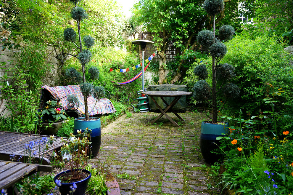 Example of an eclectic backyard stone patio design in London with no cover