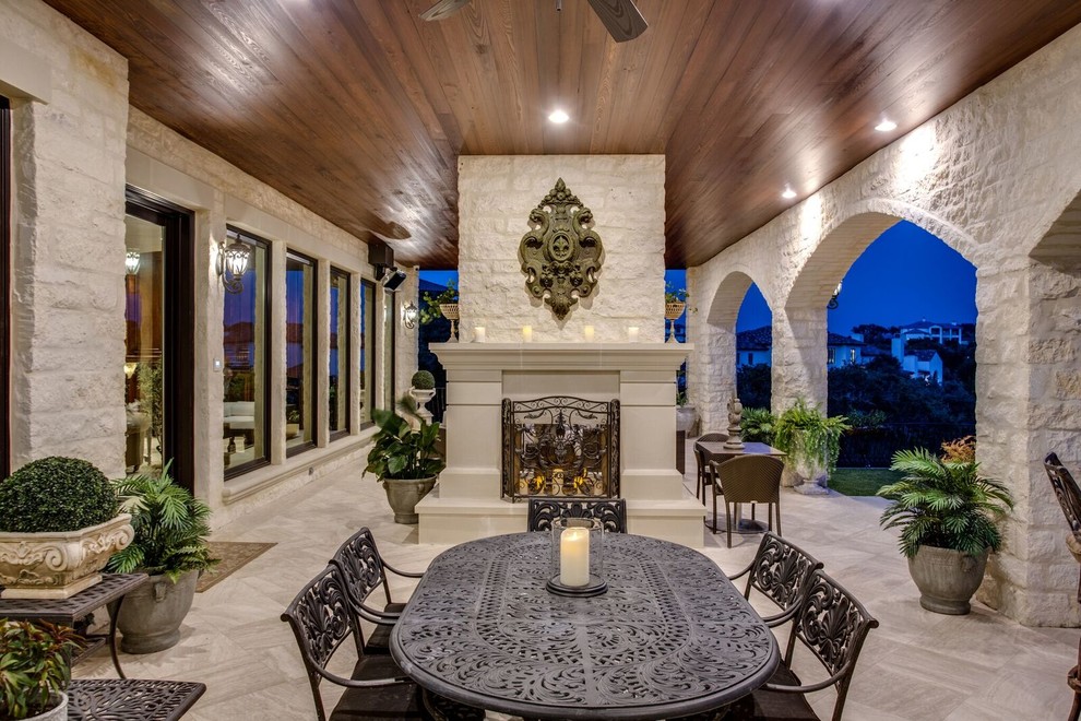 Example of a large tuscan backyard tile patio design in Austin with a roof extension and a fireplace