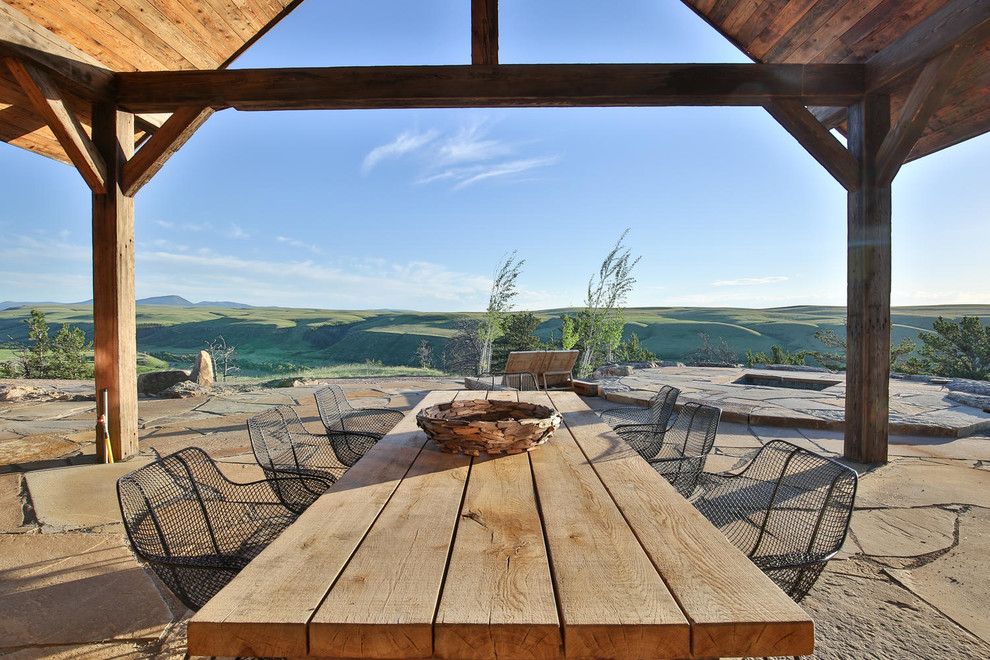 Inspiration pour une grande terrasse arrière chalet avec un foyer extérieur, des pavés en pierre naturelle et une extension de toiture.