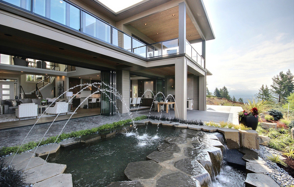 Immagine di un ampio patio o portico design dietro casa con fontane, cemento stampato e un tetto a sbalzo