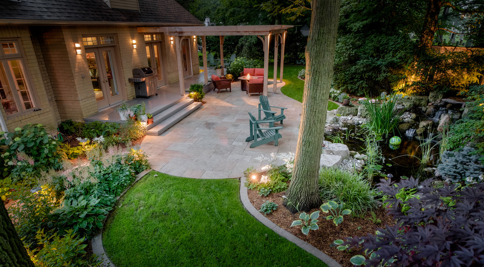 Idée de décoration pour une grande terrasse arrière tradition avec un foyer extérieur, des pavés en pierre naturelle et une pergola.