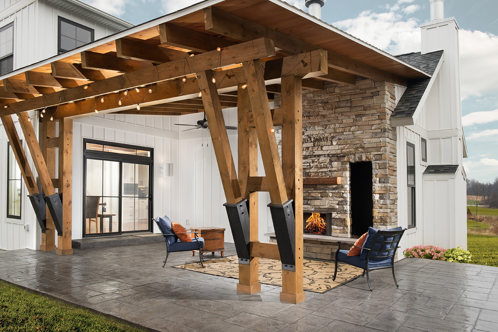 Immagine di un grande patio o portico country dietro casa con un caminetto, un tetto a sbalzo e cemento stampato