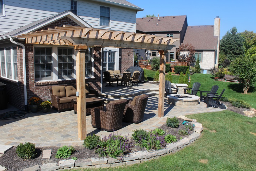 This is an example of a large classic back patio in Indianapolis with a fire feature, brick paving and a pergola.