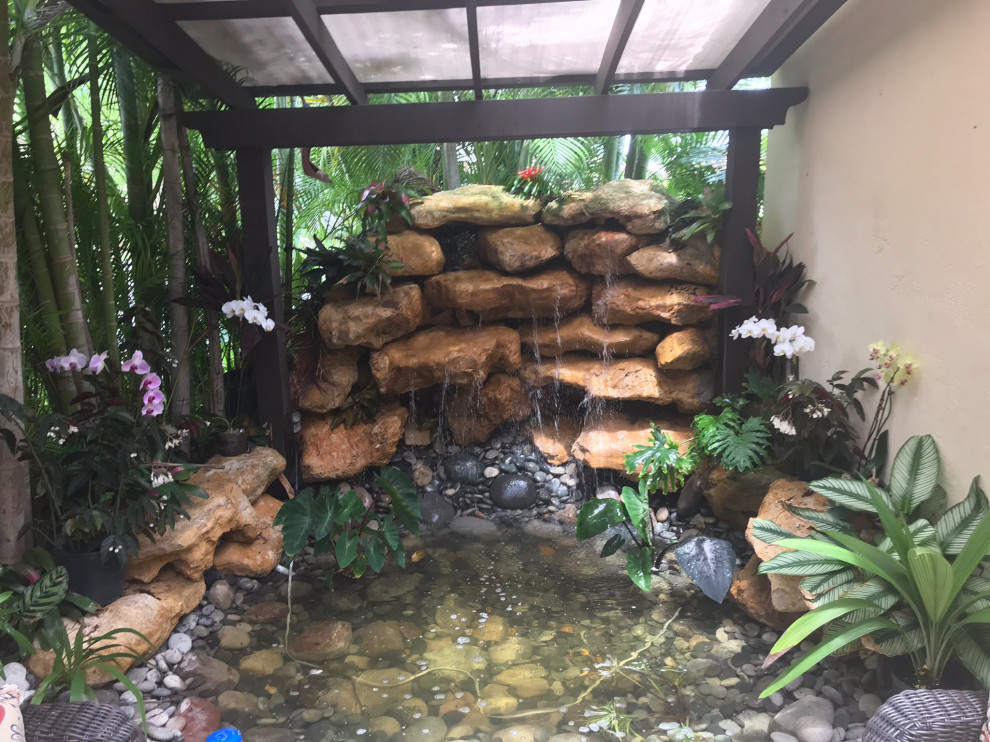 Small world-inspired back patio in Miami with a water feature, natural stone paving and a pergola.