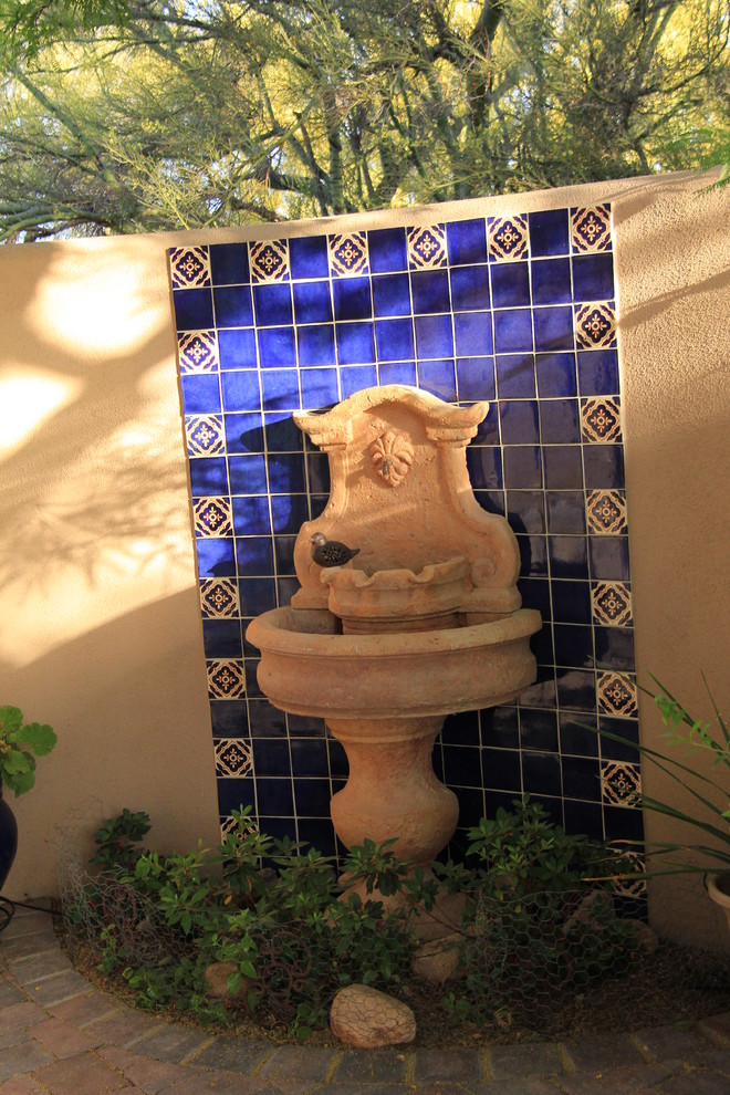 Ejemplo de patio mediterráneo de tamaño medio sin cubierta en patio trasero con fuente y adoquines de ladrillo