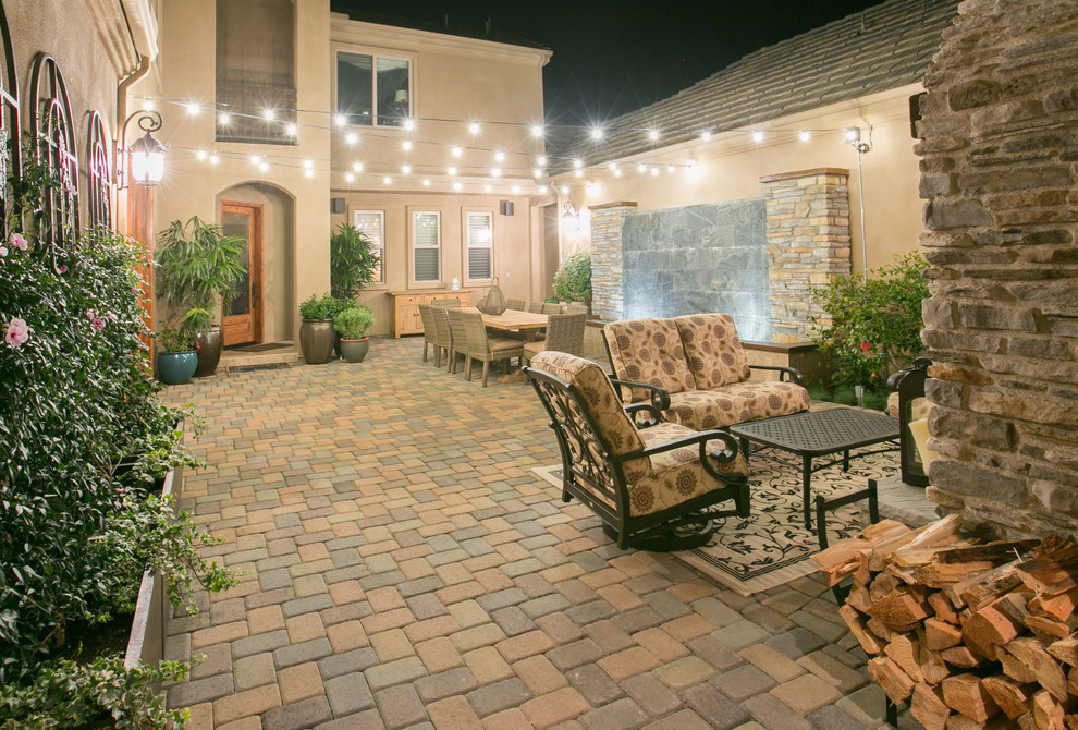 This is an example of a large classic back patio in San Diego with a water feature, concrete paving and a roof extension.