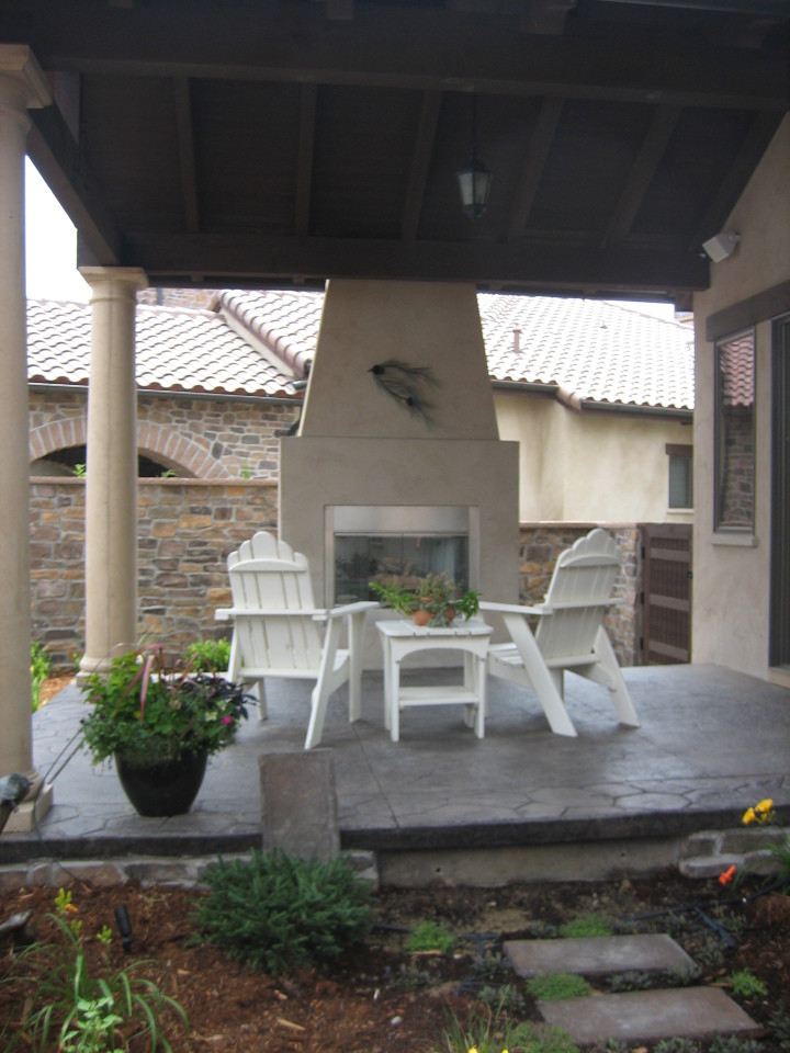 Immagine di un piccolo patio o portico mediterraneo dietro casa con un focolare, cemento stampato e un tetto a sbalzo