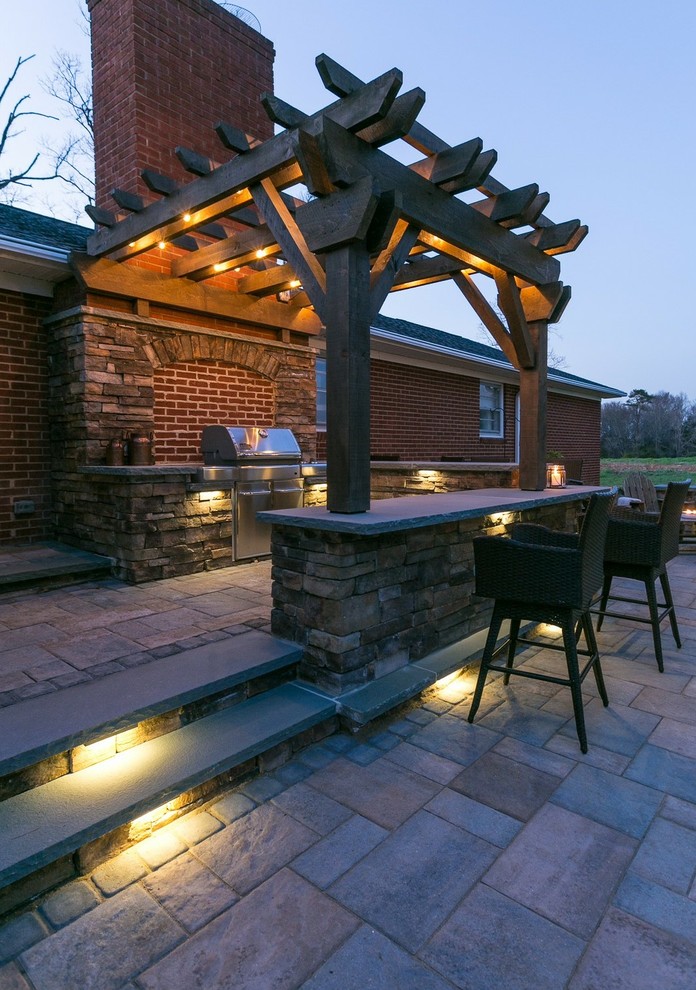 Modelo de patio campestre de tamaño medio en patio trasero con cocina exterior, adoquines de hormigón y pérgola