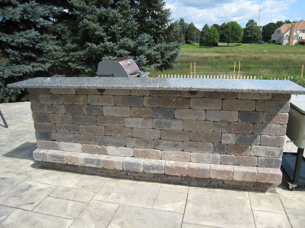 Cette image montre une grande terrasse arrière design avec une cuisine d'été et des pavés en brique.