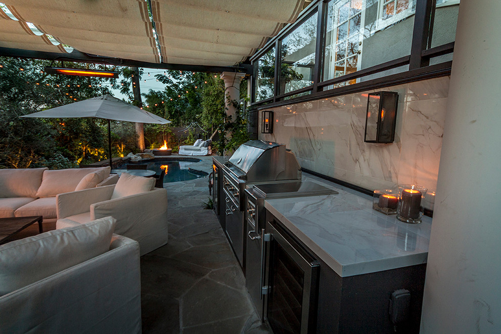 Cette photo montre une grande terrasse arrière moderne avec une cuisine d'été, des pavés en pierre naturelle et une pergola.