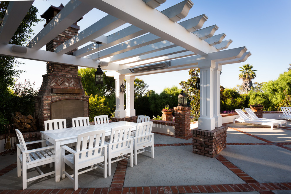 This is an example of a large traditional back patio in Orange County with a fireplace, concrete paving and a pergola.
