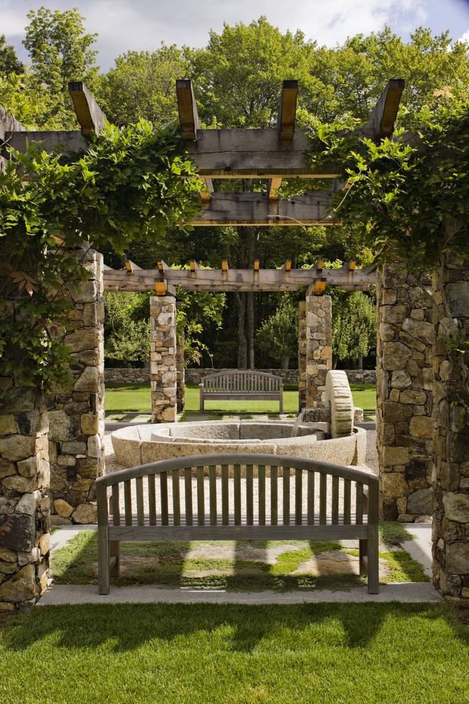 Cette image montre une grande terrasse chalet avec un point d'eau, une cour, des pavés en pierre naturelle et une pergola.