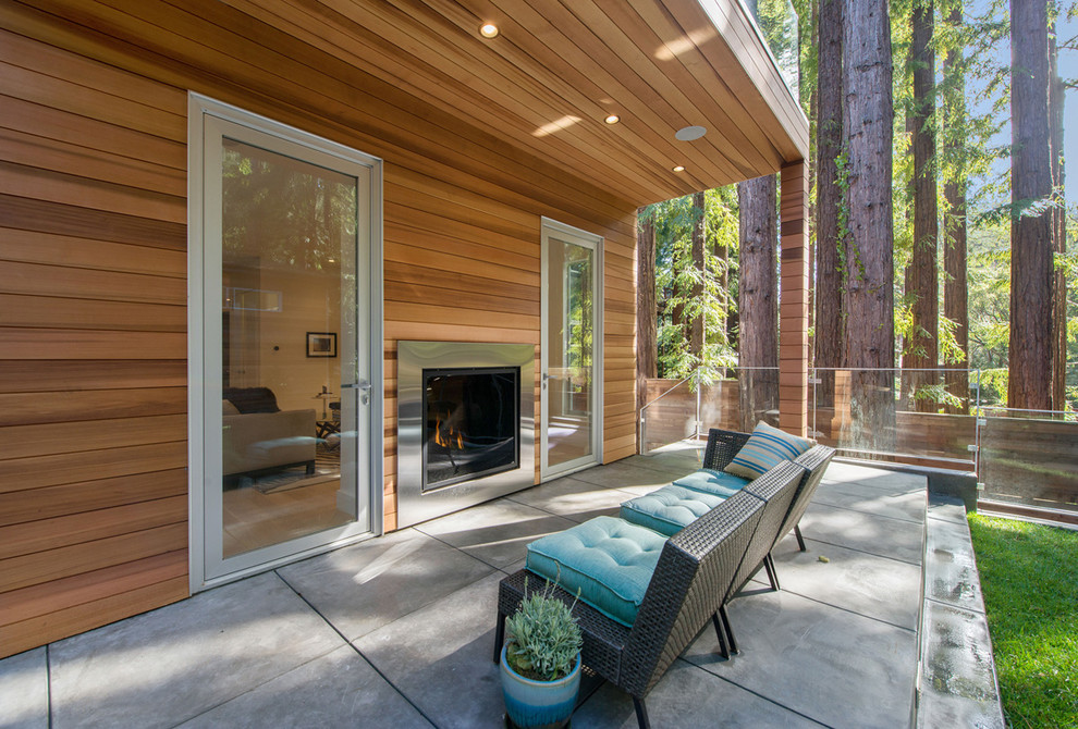 Réalisation d'une terrasse arrière design avec un foyer extérieur, une dalle de béton et une extension de toiture.