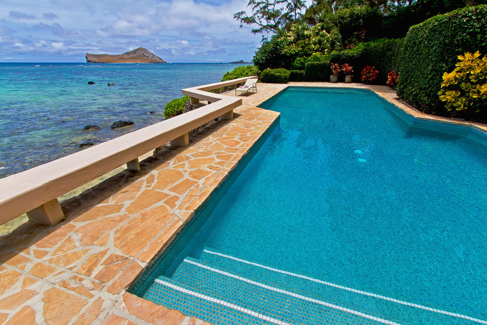 Diseño de piscina tropical grande en patio trasero con adoquines de piedra natural