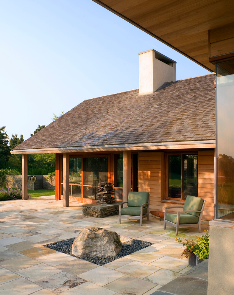 Réalisation d'une grande terrasse arrière design avec des pavés en pierre naturelle et une extension de toiture.