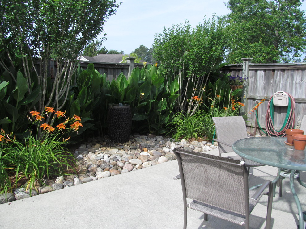 Foto de patio tropical de tamaño medio en patio trasero con fuente, gravilla y toldo