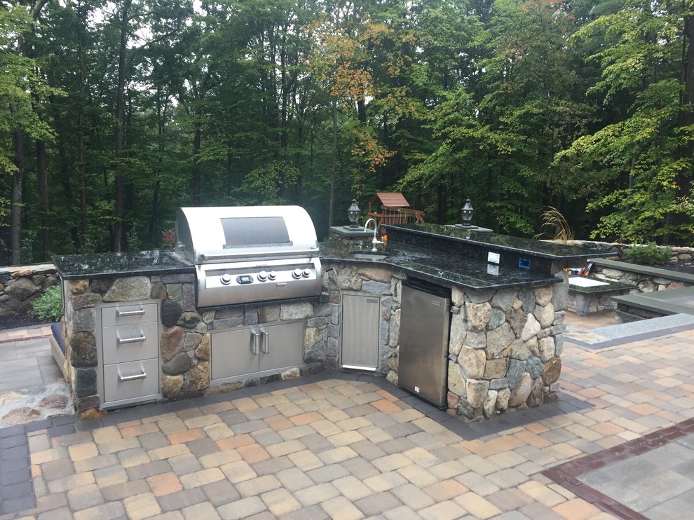 This is an example of a medium sized traditional back patio in Boston with an outdoor kitchen, brick paving and no cover.