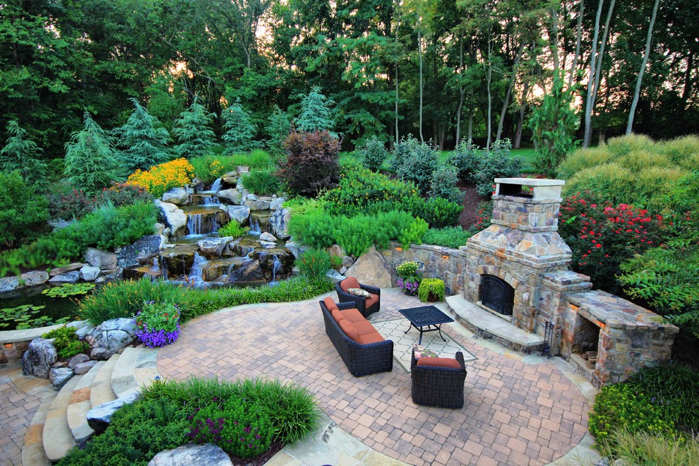 Modelo de patio clásico grande en patio trasero con adoquines de ladrillo y chimenea
