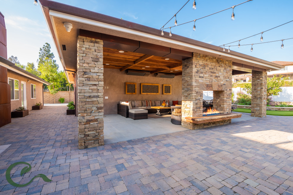 Inspiration for a large transitional backyard stone patio remodel in Orange County with a fireplace and a roof extension