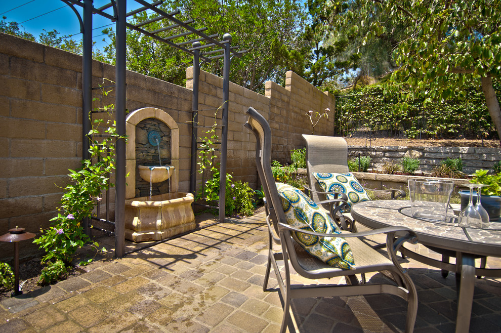Diseño de patio mediterráneo de tamaño medio en patio trasero con fuente y adoquines de hormigón