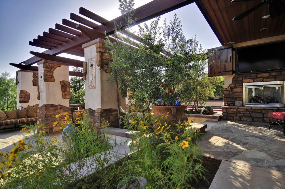 Foto di un grande patio o portico mediterraneo dietro casa con un caminetto, pavimentazioni in pietra naturale e un tetto a sbalzo