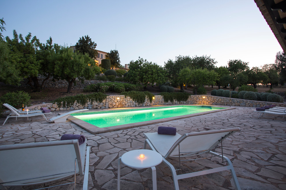 Large rural back rectangular lengths swimming pool in Palma de Mallorca with a pool house and natural stone paving.