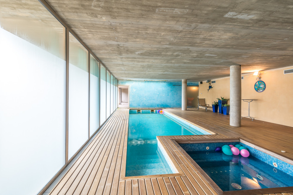 Réalisation d'une piscine intérieure design rectangle avec un bain bouillonnant et une terrasse en bois.