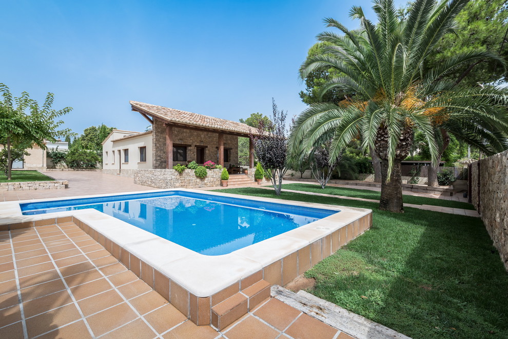 На фото: угловой, спортивный бассейн среднего размера на заднем дворе в средиземноморском стиле с домиком у бассейна и покрытием из плитки