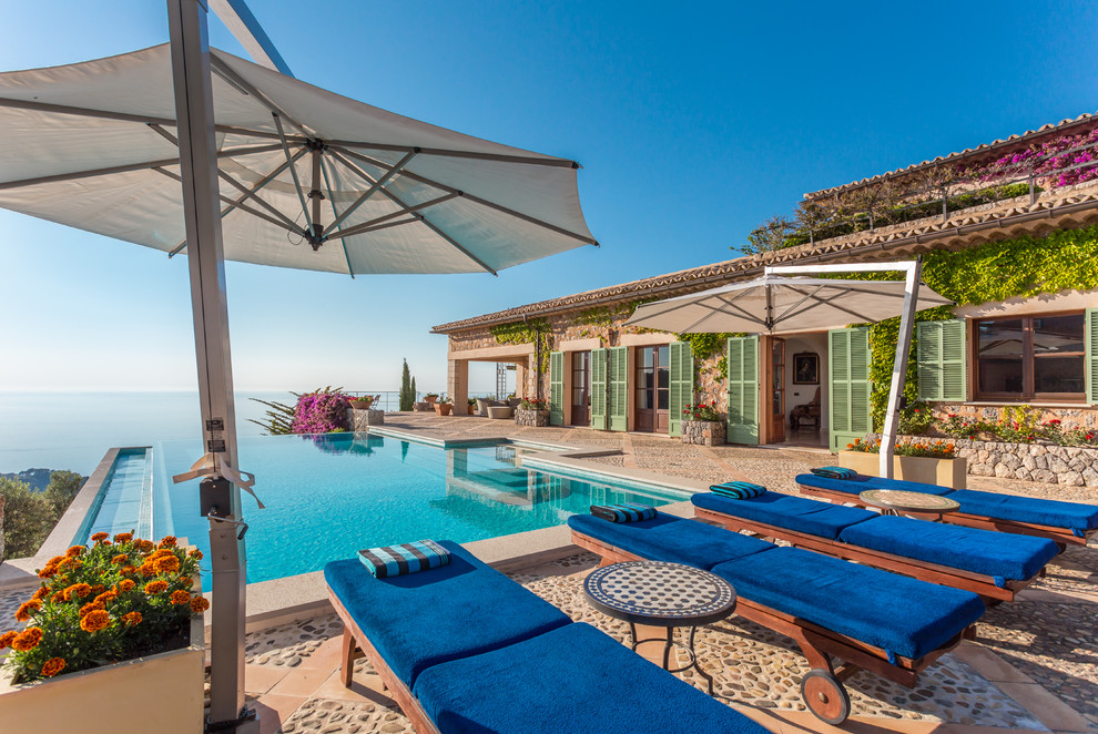 Foto de piscina infinita mediterránea grande rectangular en patio con adoquines de piedra natural
