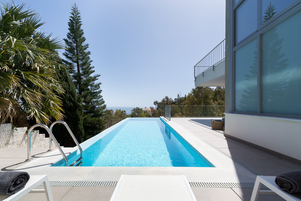 Imagen de piscina alargada actual rectangular en patio trasero con losas de hormigón
