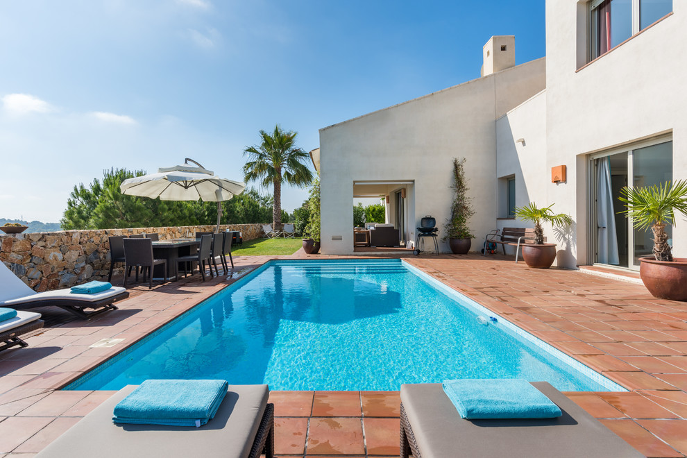 Diseño de piscina alargada mediterránea rectangular en patio trasero con suelo de baldosas