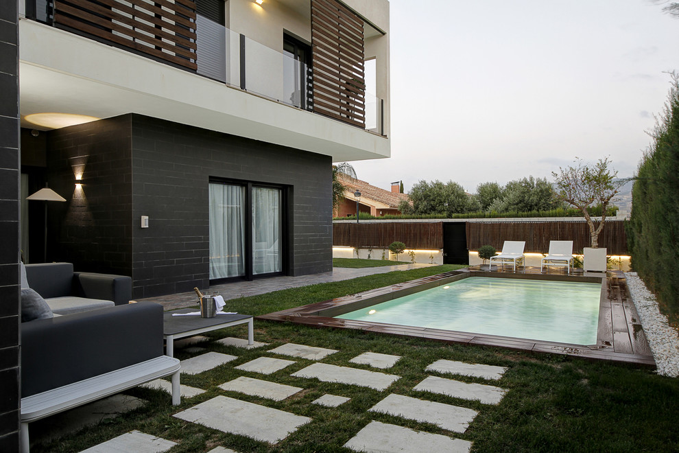Diseño de piscina alargada moderna rectangular en patio trasero con adoquines de hormigón