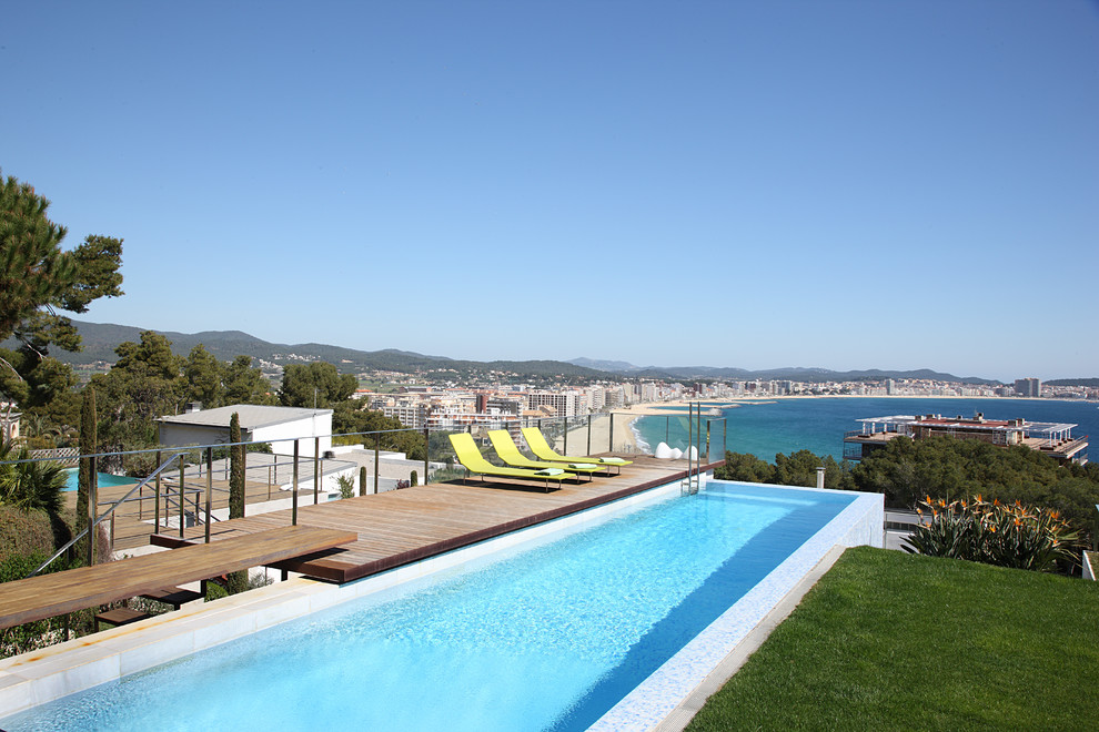 Cette image montre une très grande piscine à débordement et arrière design rectangle avec une terrasse en bois.