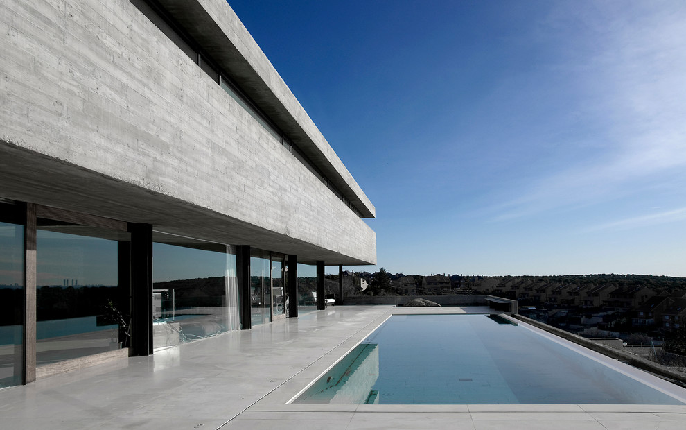 Modelo de casa de la piscina y piscina infinita minimalista grande rectangular en patio trasero con losas de hormigón
