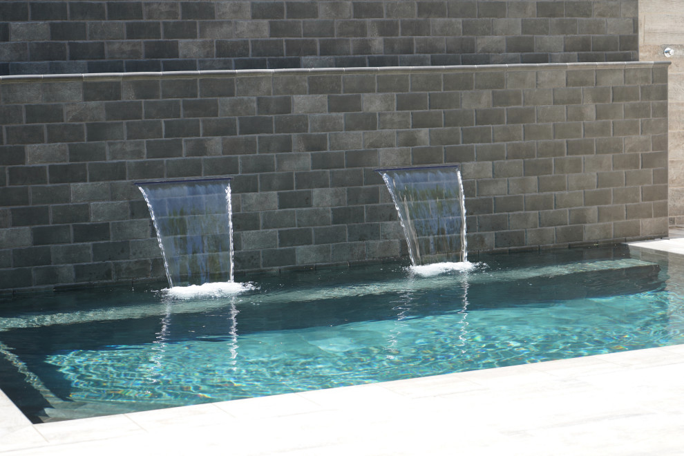Ejemplo de piscina con fuente natural tropical rectangular en patio con suelo de baldosas