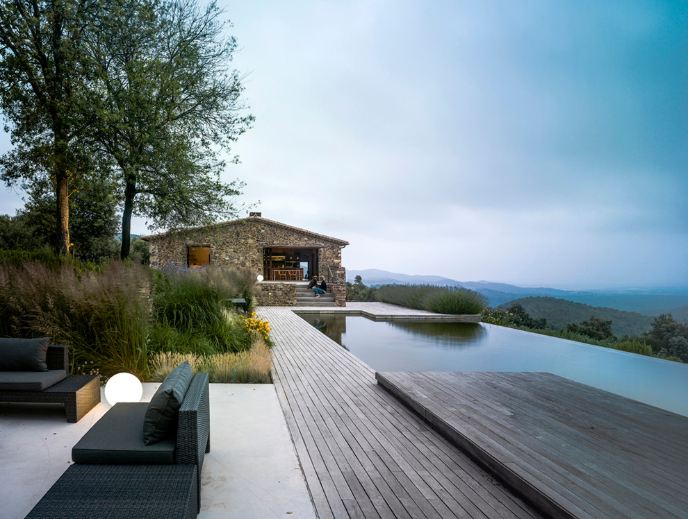 Cette photo montre une très grande piscine à débordement et arrière montagne sur mesure avec un point d'eau et une terrasse en bois.